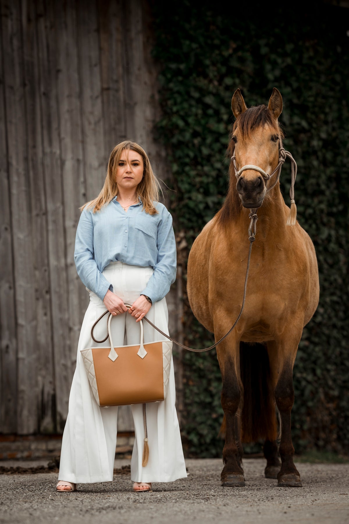 Brown Horse and Blonde woman stand next to each other. The woman carries quiet luxury handbag by alpha pajé.