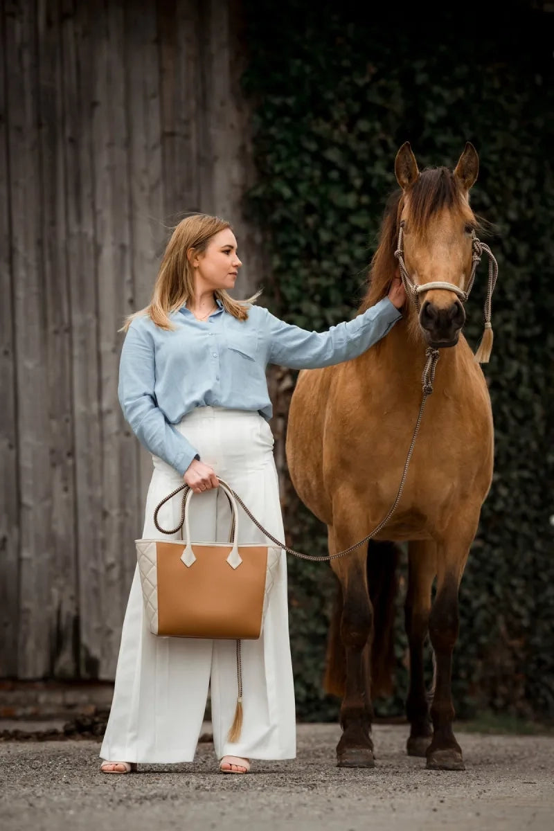 Blonde model strokes brown horse and carries quiet luxury handbag