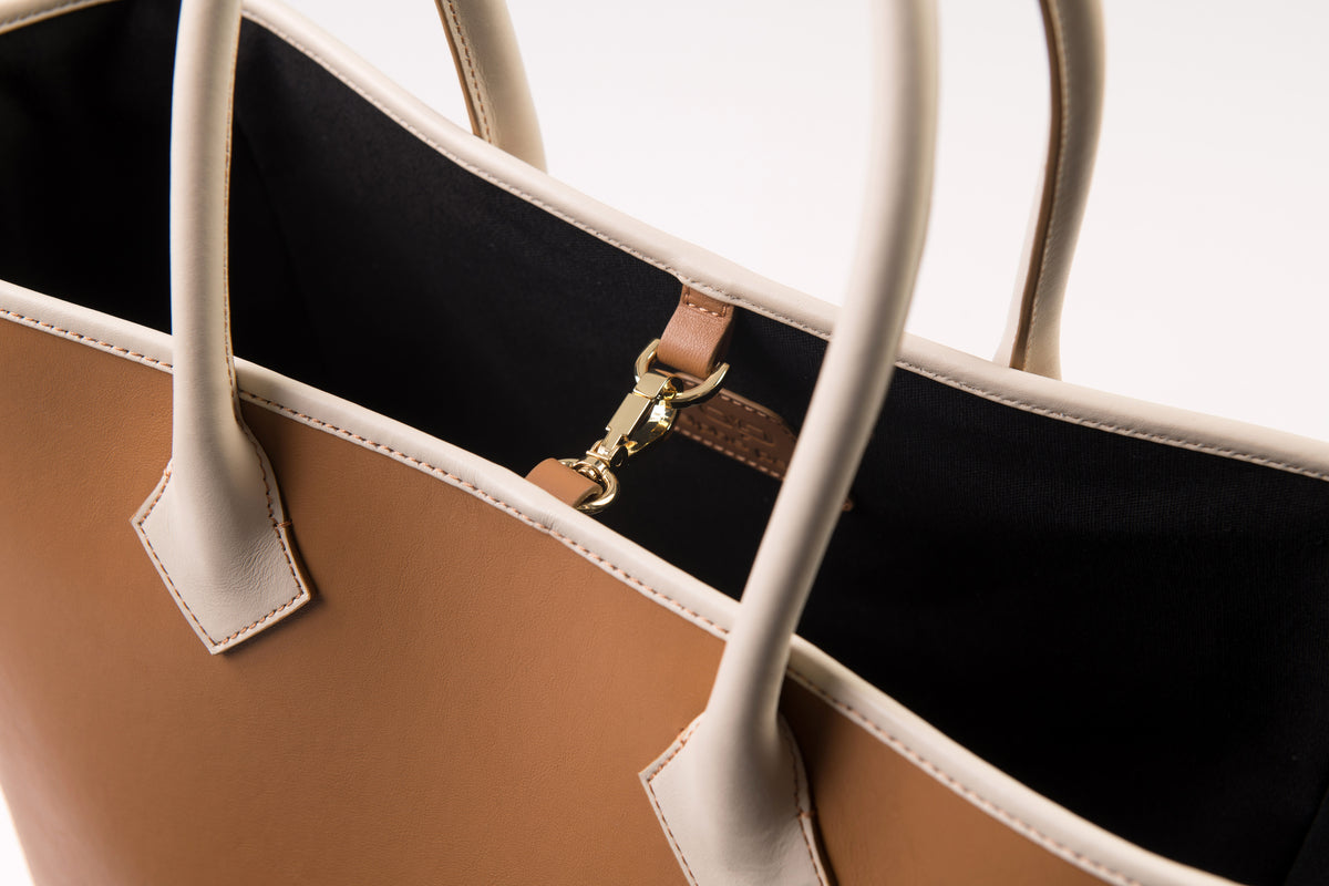 Product photo: close-up of a brown leather handbag. It has beige handles and a gold clasp.