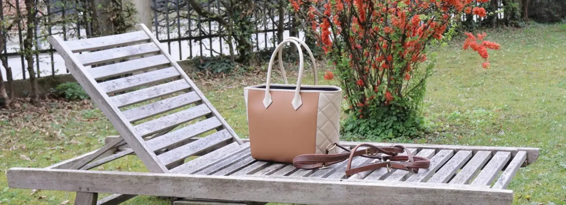 Brown luxury handbag on a garden lounger. In the background, a red flowering bush can be seen.